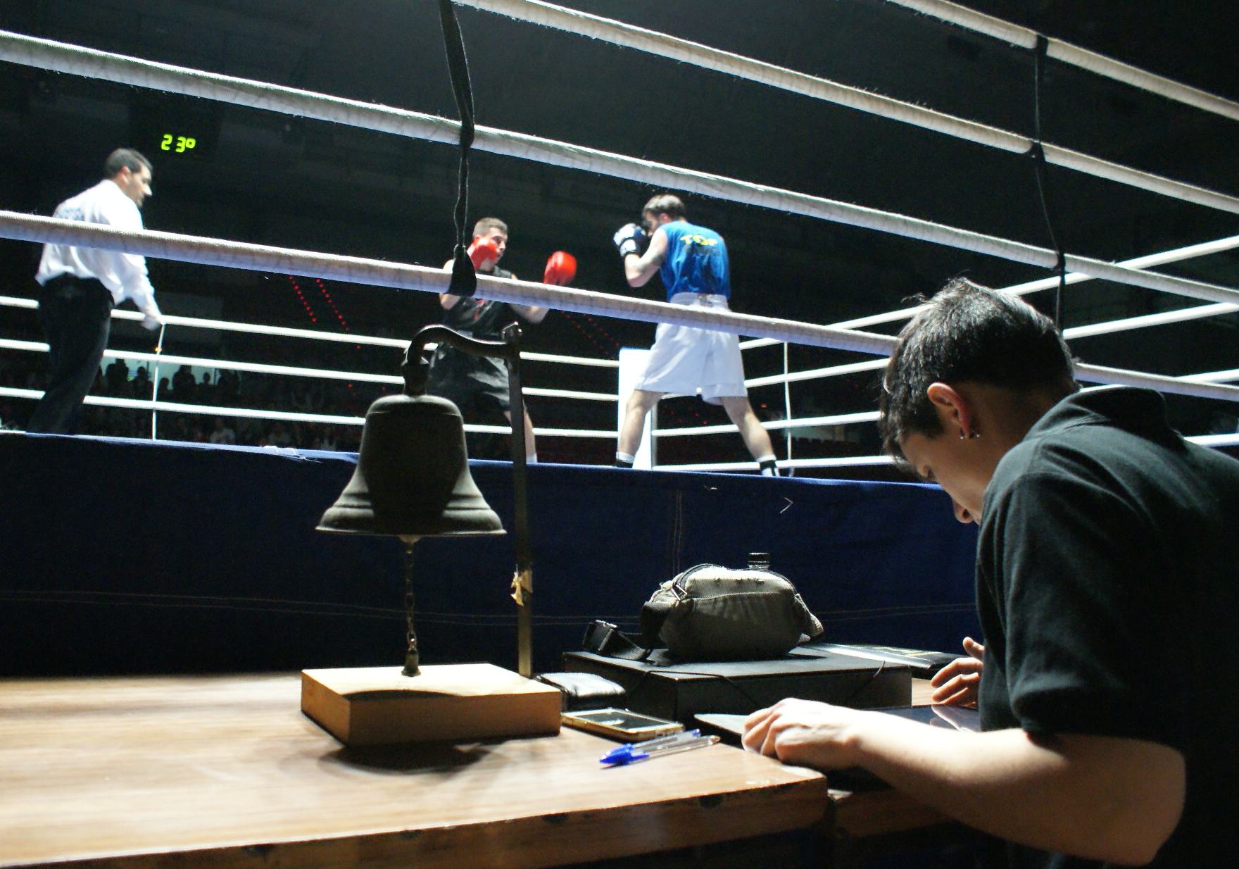 Mesa de federativos. La juez revisa documentación junto a la campana. Al fondo, boxeo, Ibon Larrinaga frente la riojano Miguel Elorza.